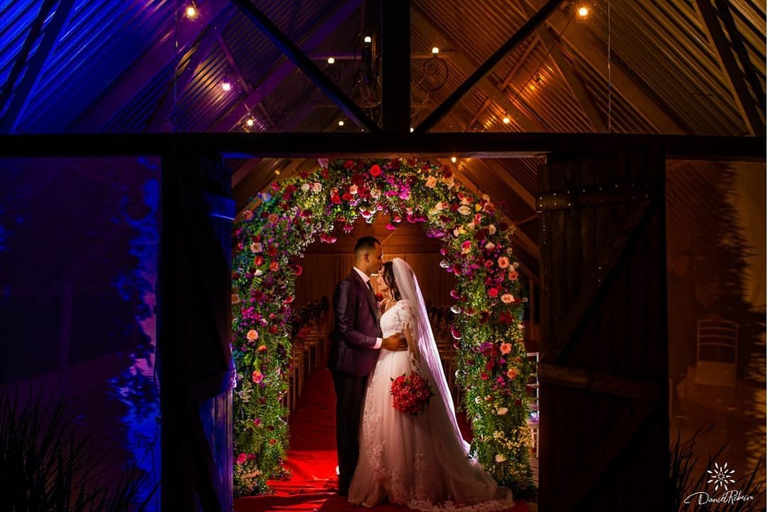 Casal sob arco de flores na cerimônia do Recanto dos Pássaros